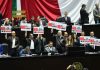 Chamber of Deputies opposition politicians hold protest signs in front of a Mexican flag