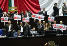 Chamber of Deputies opposition politicians hold protest signs in front of a Mexican flag