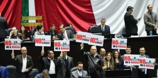 Chamber of Deputies opposition politicians hold protest signs in front of a Mexican flag