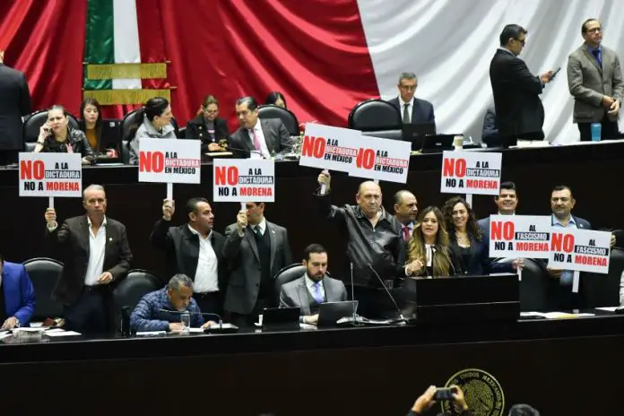 Chamber of Deputies opposition politicians hold protest signs in front of a Mexican flag