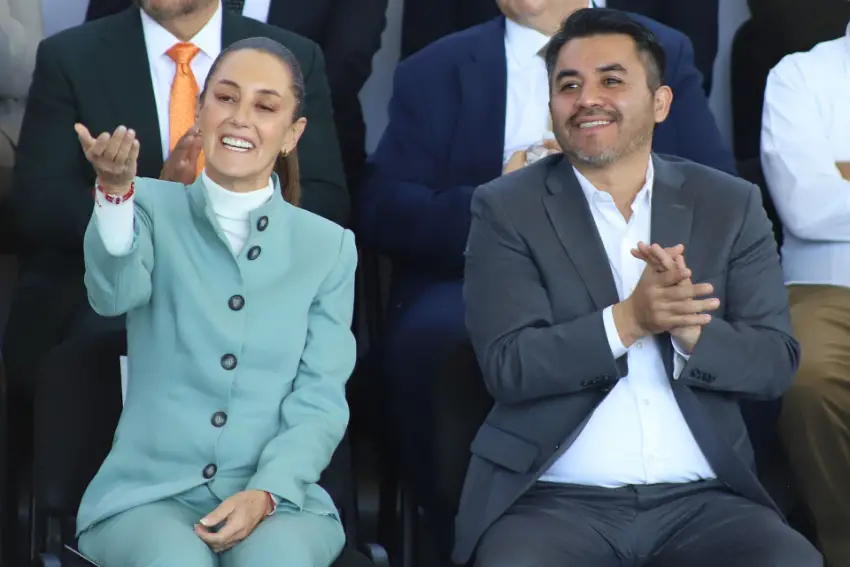 President Claudia Sheinbaum sitting with National Water Commission director Efraín Morales. Sheinbaum is holding her hand up, palm upward, in a gesture at someone off camera. Morales is clapping and also looking at someone off camera.