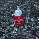 A member of Greenpeace Mexico stands on a mountain of trash at the Coatzacoalcos landfill wearing a hazmat suit with a sign reading "Ley Antiplasticos YA!"