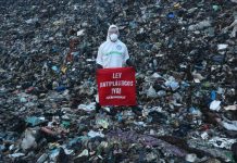 A member of Greenpeace Mexico stands on a mountain of trash at the Coatzacoalcos landfill wearing a hazmat suit with a sign reading "Ley Antiplasticos YA!"