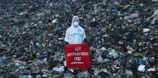 A member of Greenpeace Mexico stands on a mountain of trash at the Coatzacoalcos landfill wearing a hazmat suit with a sign reading "Ley Antiplasticos YA!"