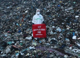 A member of Greenpeace Mexico stands on a mountain of trash at the Coatzacoalcos landfill wearing a hazmat suit with a sign reading "Ley Antiplasticos YA!"