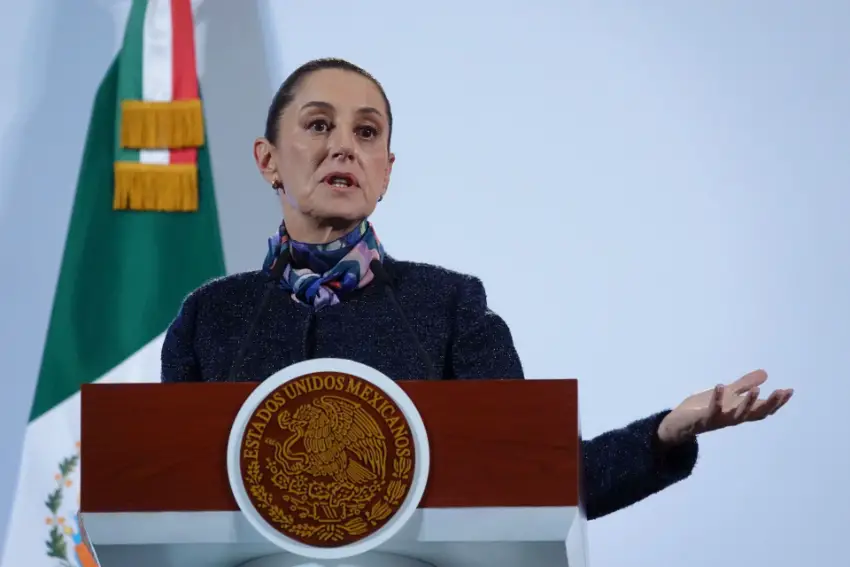 Mexico's President Claudia Sheinbaum gesturing with one hand out, palm upward, as she stands at the presidential podium making a point during a press conference.