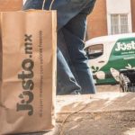 A delivery person from Mexican company Jüsto holds a pair of paper bags