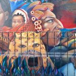 Street mural featuring the larger-than-life heads of Mexican and Mexican indigenous women, as well as a Mexican man wearing a traditional campesino garb, and another man in a jaguar headdress.