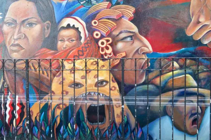 Street mural featuring the larger-than-life heads of Mexican and Mexican indigenous women, as well as a Mexican man wearing a traditional campesino garb, and another man in a jaguar headdress.