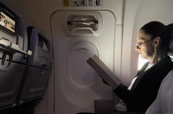 Mexico's President Claudia Sheinbaum sitting in a commercial flight looking at an e-reader as she heads from Mexico to the 2024 G20 Leaders' Summit