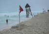 People in the water on a Cancun beach. On the beach near the shore is a red advisory flag warning of strong currents