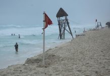 People in the water on a Cancun beach. On the beach near the shore is a red advisory flag warning of strong currents