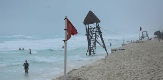 People in the water on a Cancun beach. On the beach near the shore is a red advisory flag warning of strong currents