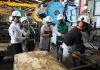 Workers in lab coats and hard hats watch another worker in a Mexican factory