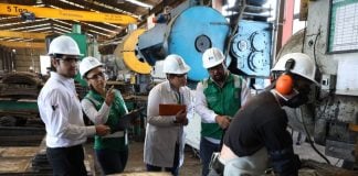 Workers in lab coats and hard hats watch another worker in a Mexican factory