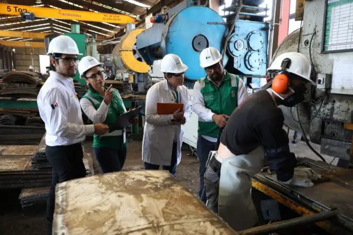 Workers in lab coats and hard hats watch another worker in a Mexican factory