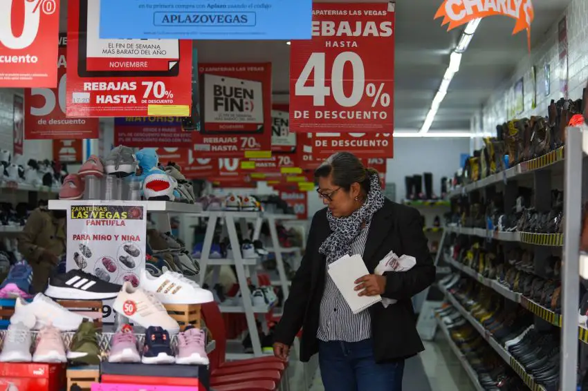 A shopper looks at shoes in a store filled with Buen Fin discount advertisements