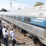 A crowd welcomes a passenger train that speeds into a station