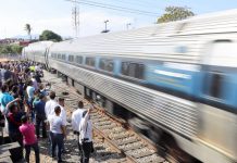 A crowd welcomes a passenger train that speeds into a station