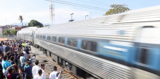 A crowd welcomes a passenger train that speeds into a station