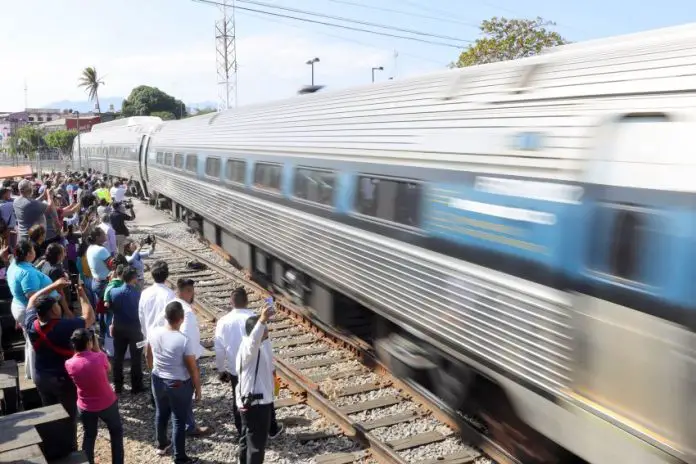 A crowd welcomes a passenger train that speeds into a station