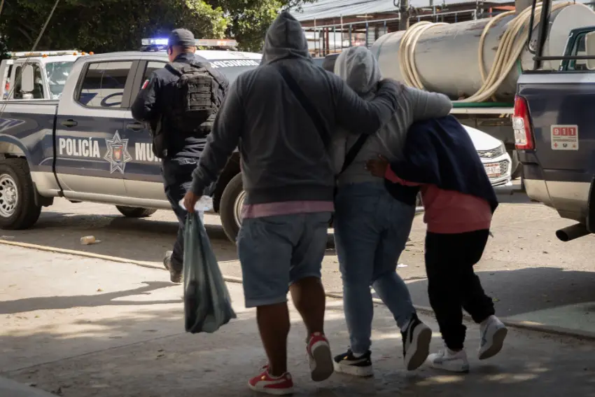 Migrants huddled together as they walk in Tijuana near a municipal police truck