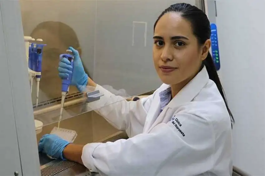 Young woman in a lab coat and scientific lab research equipment in her hands. She is wearing latex gloves and staring at the camera