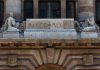 The top of the facade of the Bank of Mexico building in Mexico City, which features a sculptured man and woman in ancient Roman-style dress on either side of a block of stone saying Banco de Mexico