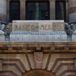 The top of the facade of the Bank of Mexico building in Mexico City, which features a sculptured man and woman in ancient Roman-style dress on either side of a block of stone saying Banco de Mexico
