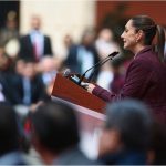 Claudia Sheinbaum at a podium addressing a crowd of Mexican legislators in Mexico's National Palace