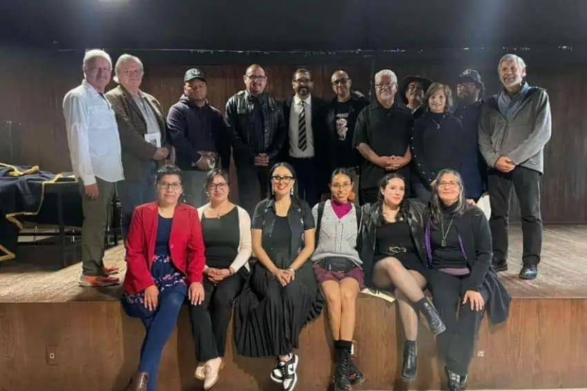 A group of academics and some college students dressed casually posing formally for a photo in a small auditorium