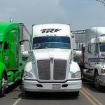 Three tractor trailers parked, completely blocking a major roadway. From elft to right, they are lime green, white and white.