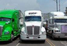 Three tractor trailers parked, completely blocking a major roadway. From elft to right, they are lime green, white and white.