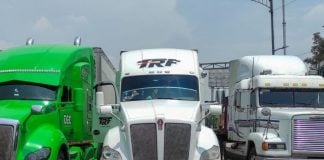 Three tractor trailers parked, completely blocking a major roadway. From elft to right, they are lime green, white and white.