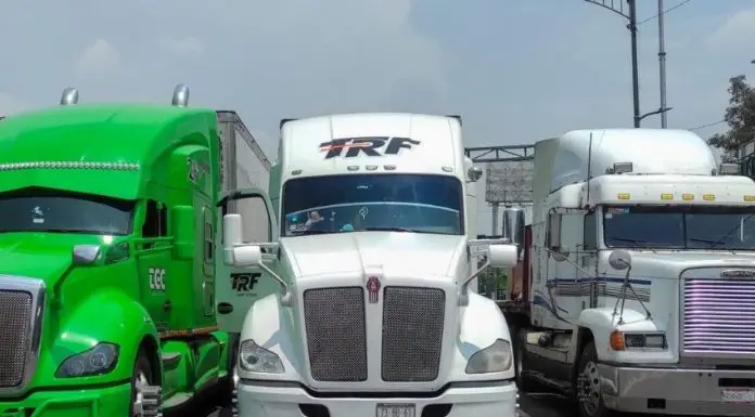 Three tractor trailers parked, completely blocking a major roadway. From elft to right, they are lime green, white and white.