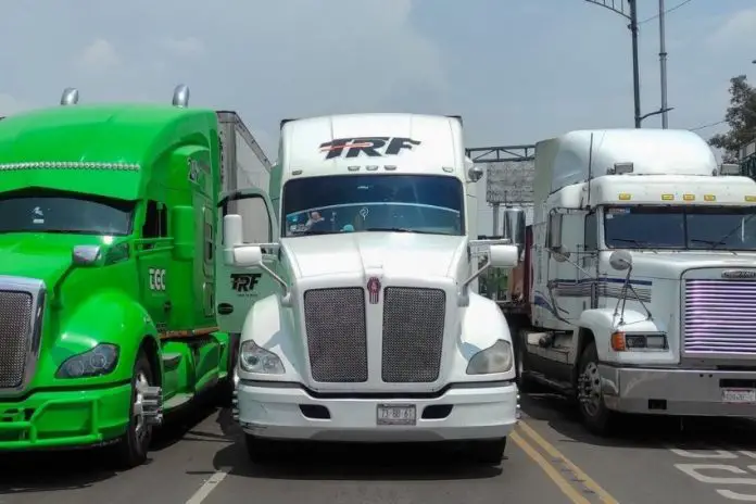 Three tractor trailers parked, completely blocking a major roadway. From elft to right, they are lime green, white and white.