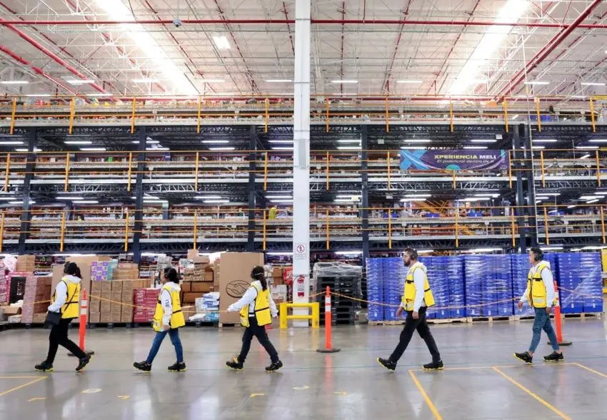 Mercado Libre employees walk in front of tall shelves in a warehouse