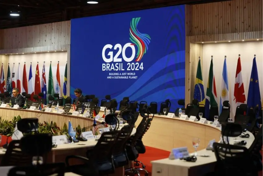 Various people sitting at conference benches at a preparation session for the G20 2024. A banner saying G20 Brasil 2024, "Building a Just World and a Sustainable Planet" is behind them, hanging on a wall.