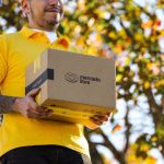 A delivery person in a yellow shirt holds a brown package with the Mercado Libre logo