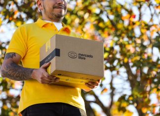 A delivery person in a yellow shirt holds a brown package with the Mercado Libre logo