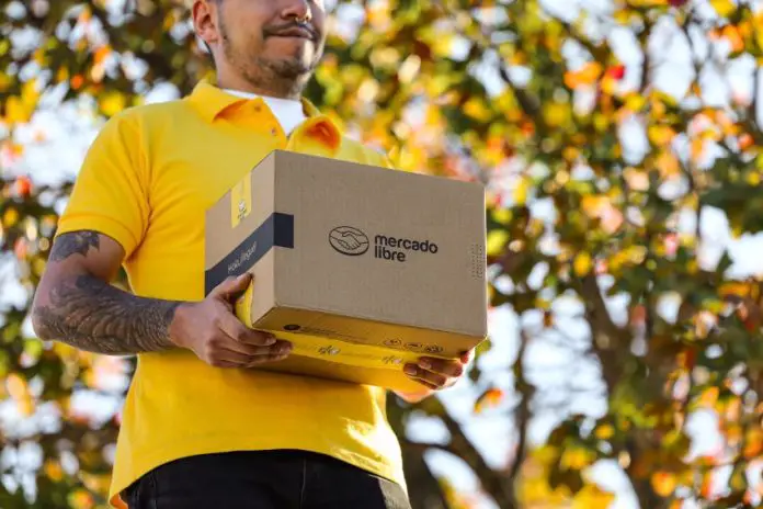 A delivery person in a yellow shirt holds a brown package with the Mercado Libre logo