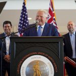 Ontario, Canada Prime Minister Doug Ford standing at a podium with the logo of the Labourers International Union of North America giving a speech. Behind him are two men watching on