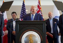 Ontario, Canada Prime Minister Doug Ford standing at a podium with the logo of the Labourers International Union of North America giving a speech. Behind him are two men watching on