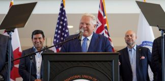 Ontario, Canada Prime Minister Doug Ford standing at a podium with the logo of the Labourers International Union of North America giving a speech. Behind him are two men watching on