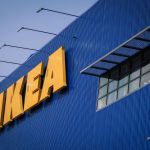 Front of an IKEA store, a blue corrugated metal facade with the yellow IKEA logo's letters in all caps in the top left of the photo.