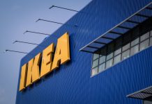 Front of an IKEA store, a blue corrugated metal facade with the yellow IKEA logo's letters in all caps in the top left of the photo.