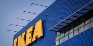 Front of an IKEA store, a blue corrugated metal facade with the yellow IKEA logo's letters in all caps in the top left of the photo.