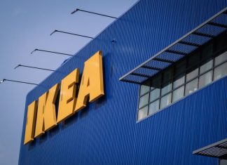 Front of an IKEA store, a blue corrugated metal facade with the yellow IKEA logo's letters in all caps in the top left of the photo.