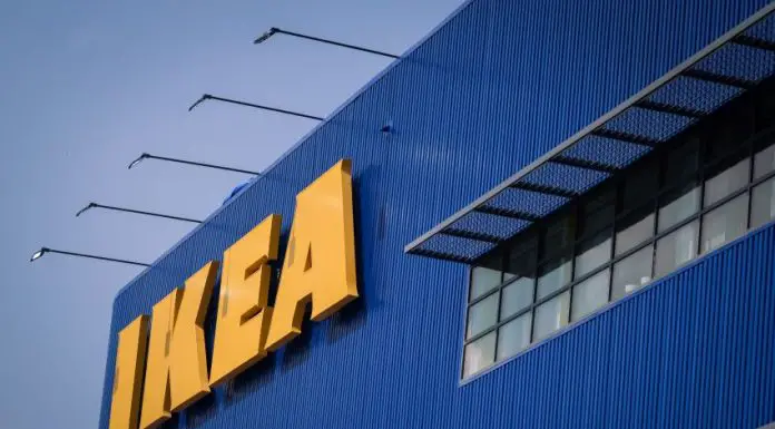 Front of an IKEA store, a blue corrugated metal facade with the yellow IKEA logo's letters in all caps in the top left of the photo.