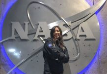 A young woman wearing a NASA jumper poses in front of a massive NASA logo